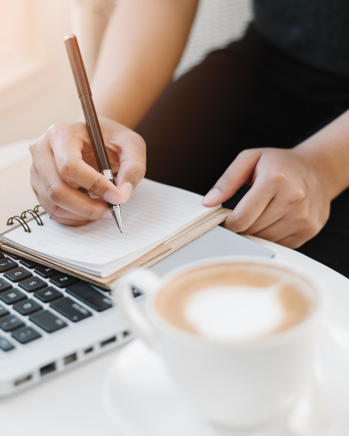 girl writing in notebook with laptop and coffee on desk