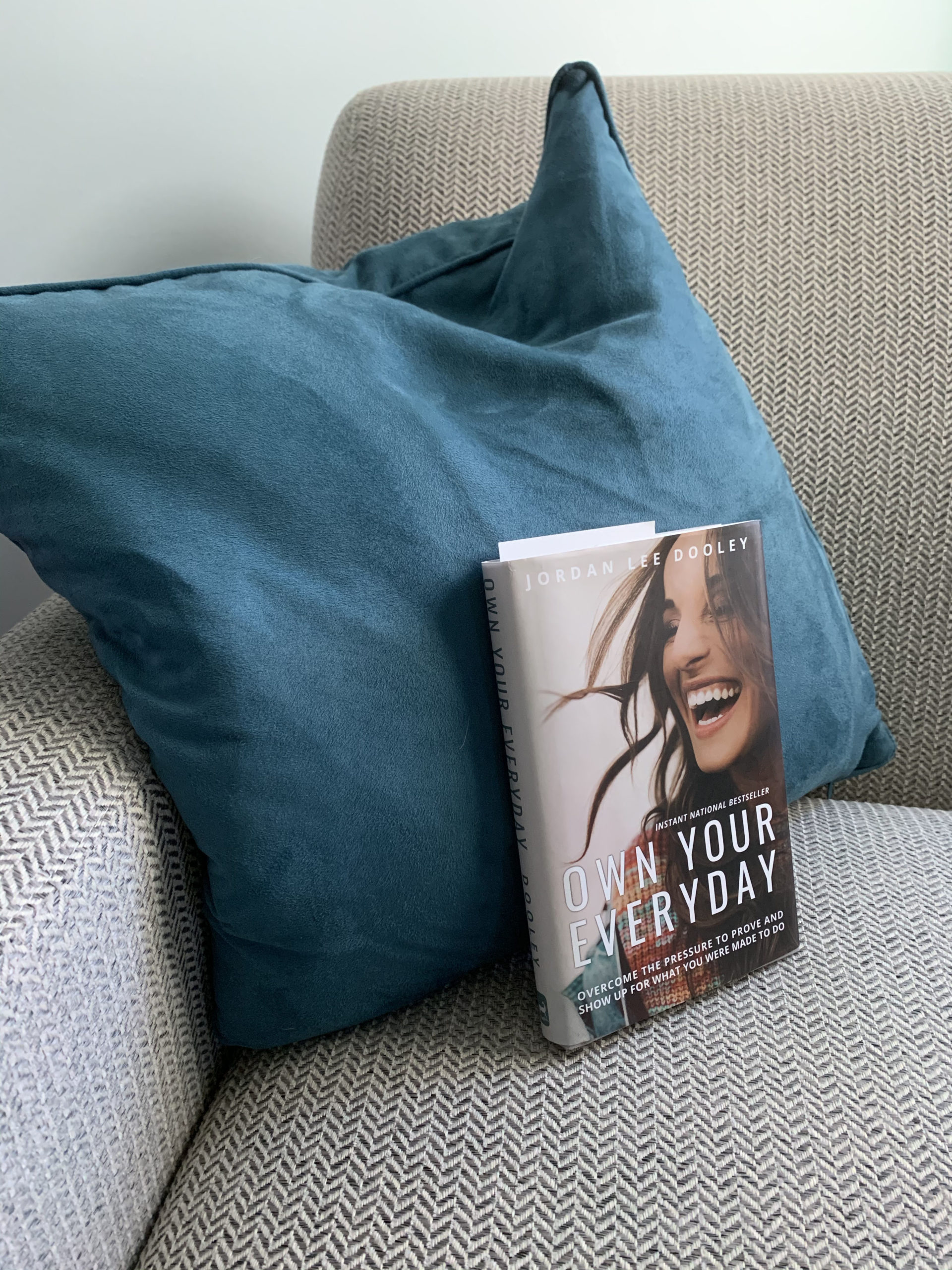 book in a tan chair with a teal pillow