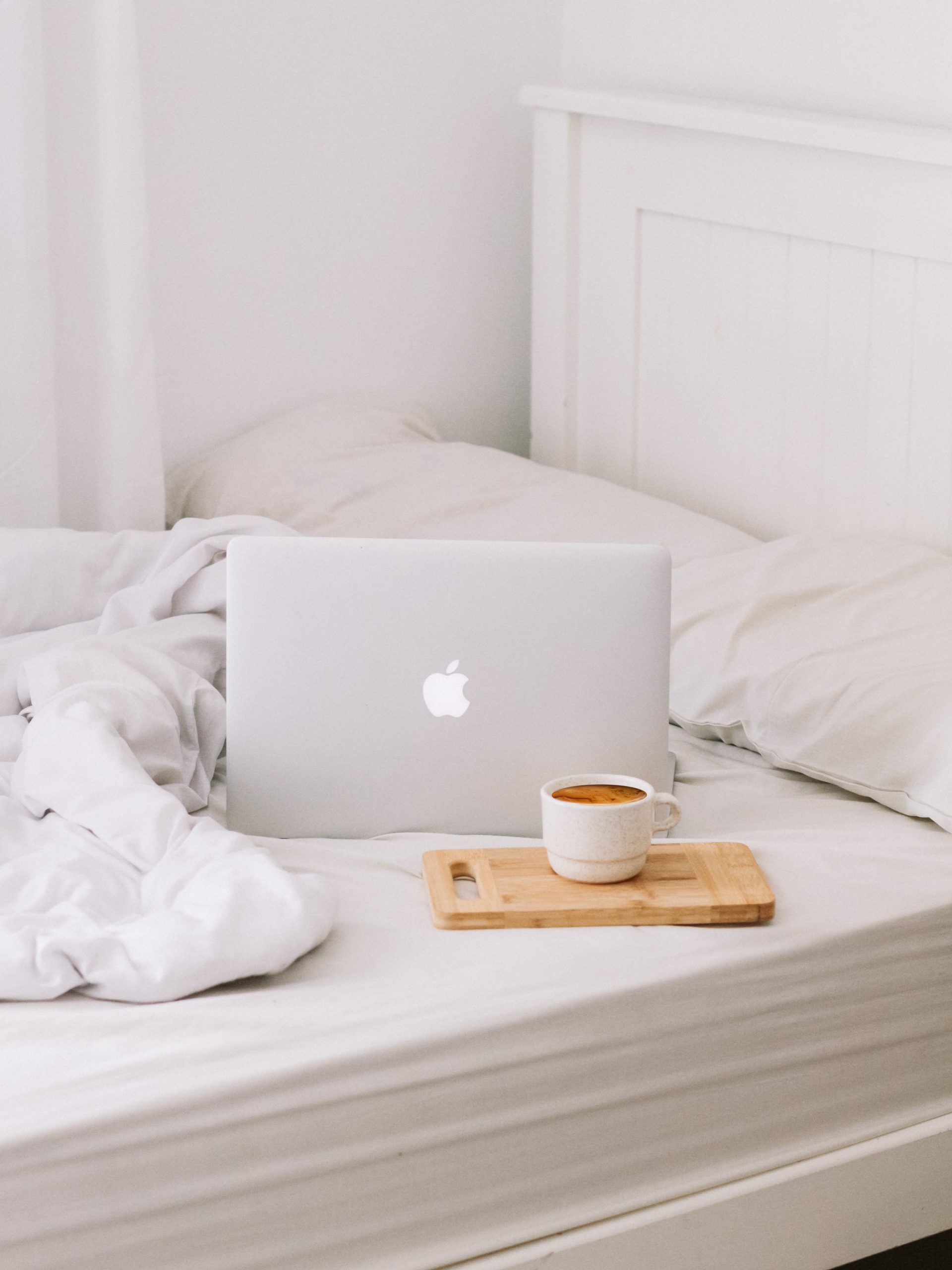 macbook laptop on bed with coffee mug