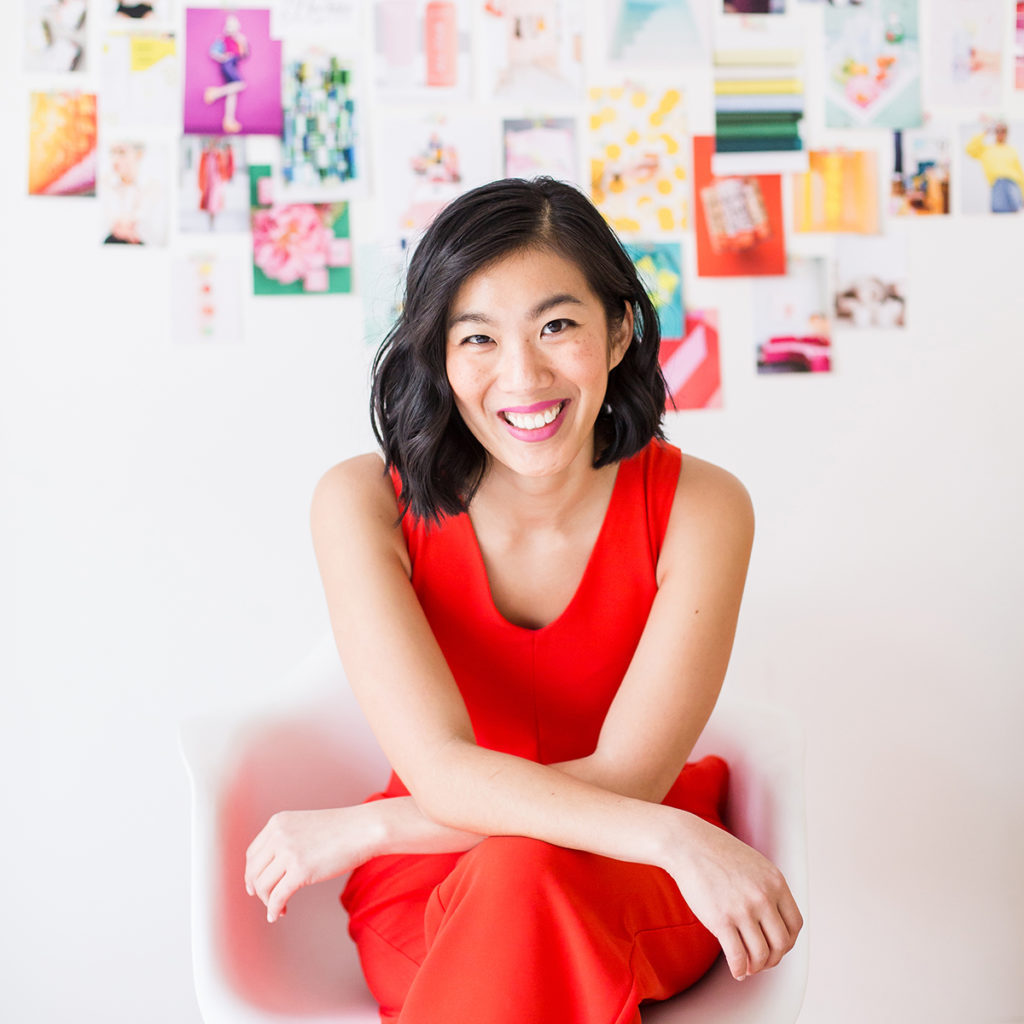 Nicole Yang - woman sitting down, smiling at the camera, wearing bright red